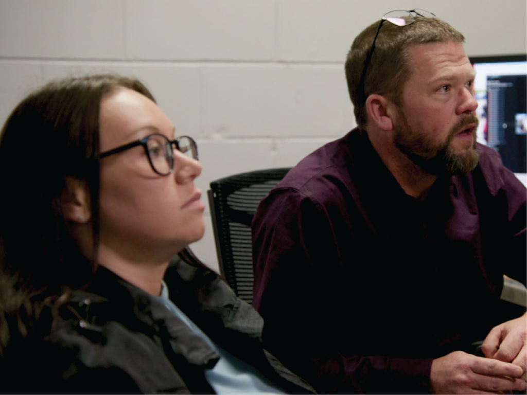 A woman with glasses sitting and a man sitting listening to a presentation