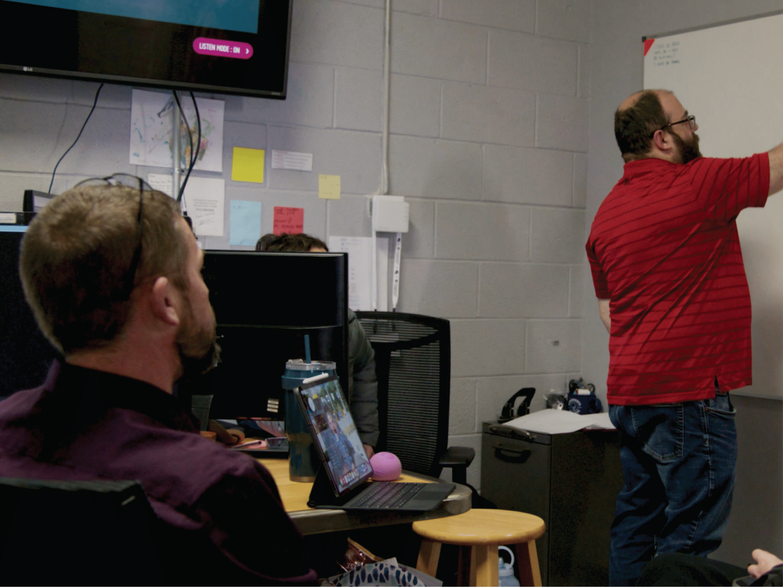 White gentleman in red shirt presenting on white board. white gentleman in purple shirt watches presentation.